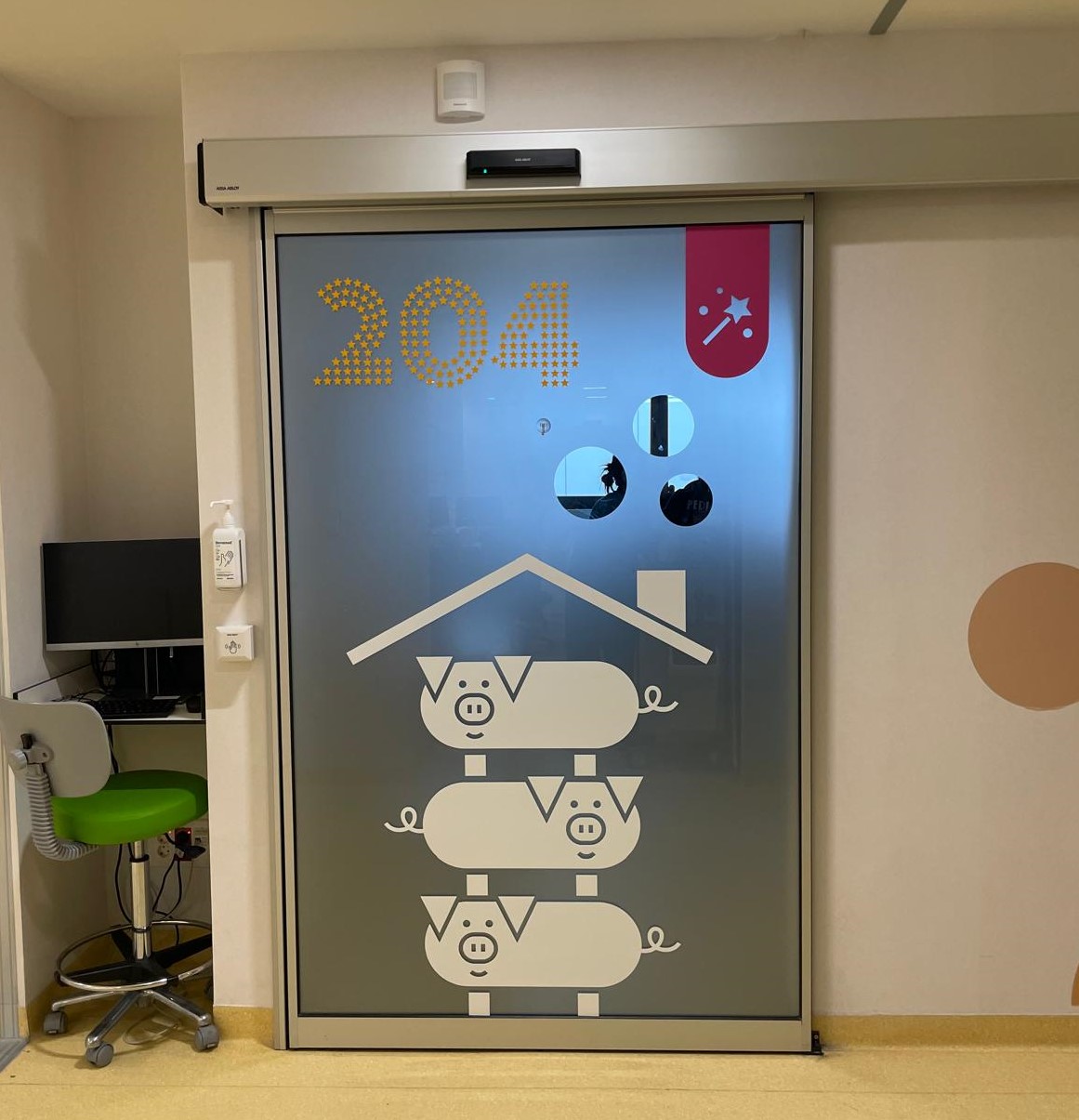 A hospital room door labeled "204" features a playful design of three cartoon pigs stacked under a roof, creating a welcoming and child-friendly atmosphere in the pediatric or neonatal unit.